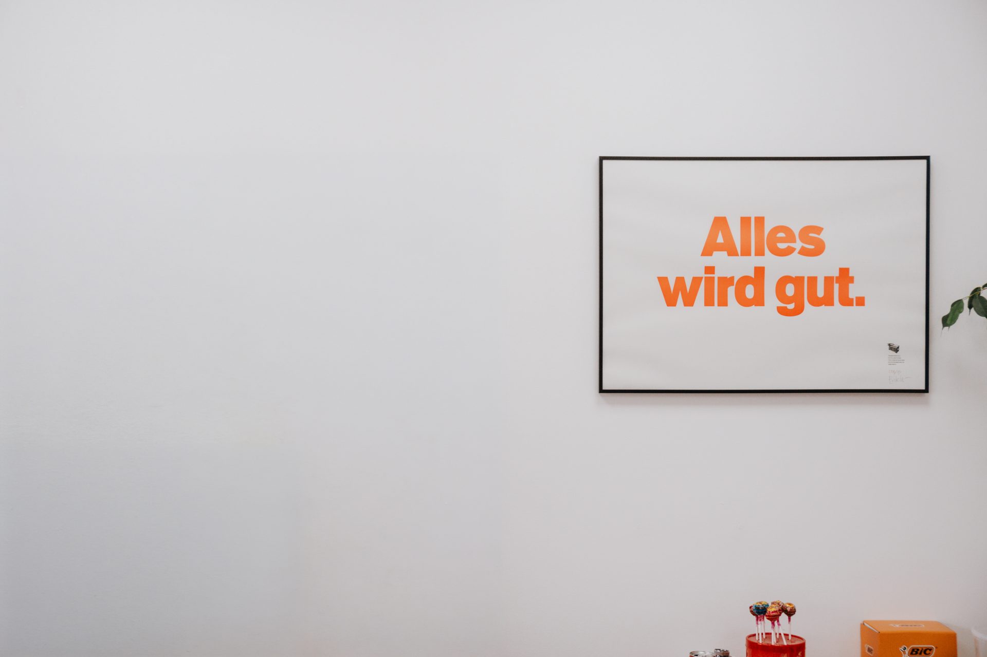 Gerahmtes Plakat mit dem Satz „Alles wird gut.“ an einer hellen Wand